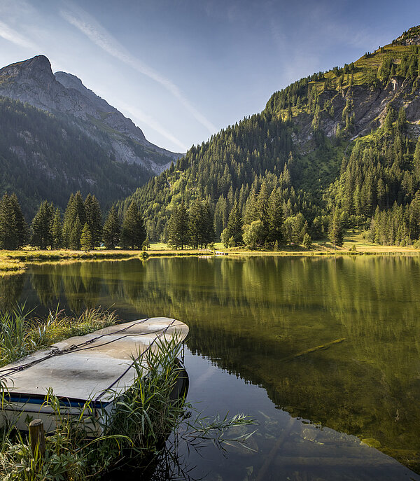 Der Lauenensee im Herbst mit Bergen im Hintergrund. Im Vordergrund ist ein Ruderboot zu sehen.