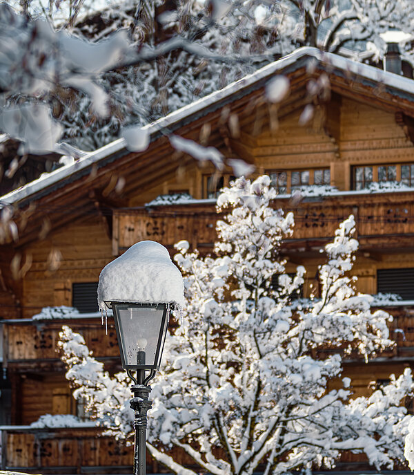 Ein typisches vierstöckiges Holzchalet mit Balkonen zwischen schneebedeckten Bäumen.