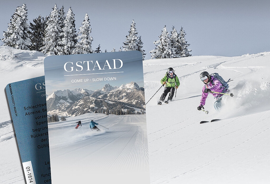 Zwei Skifahrer auf der Abfahrt durch Pulverschnee. Im Hintergrund verschneite Tannen. Im Vordergrund zwei Keycards Skidatenträger mit dem Gstaad Logo und einem Bild einer Skipiste mit Bergpanorama und zwei Skifahrern.