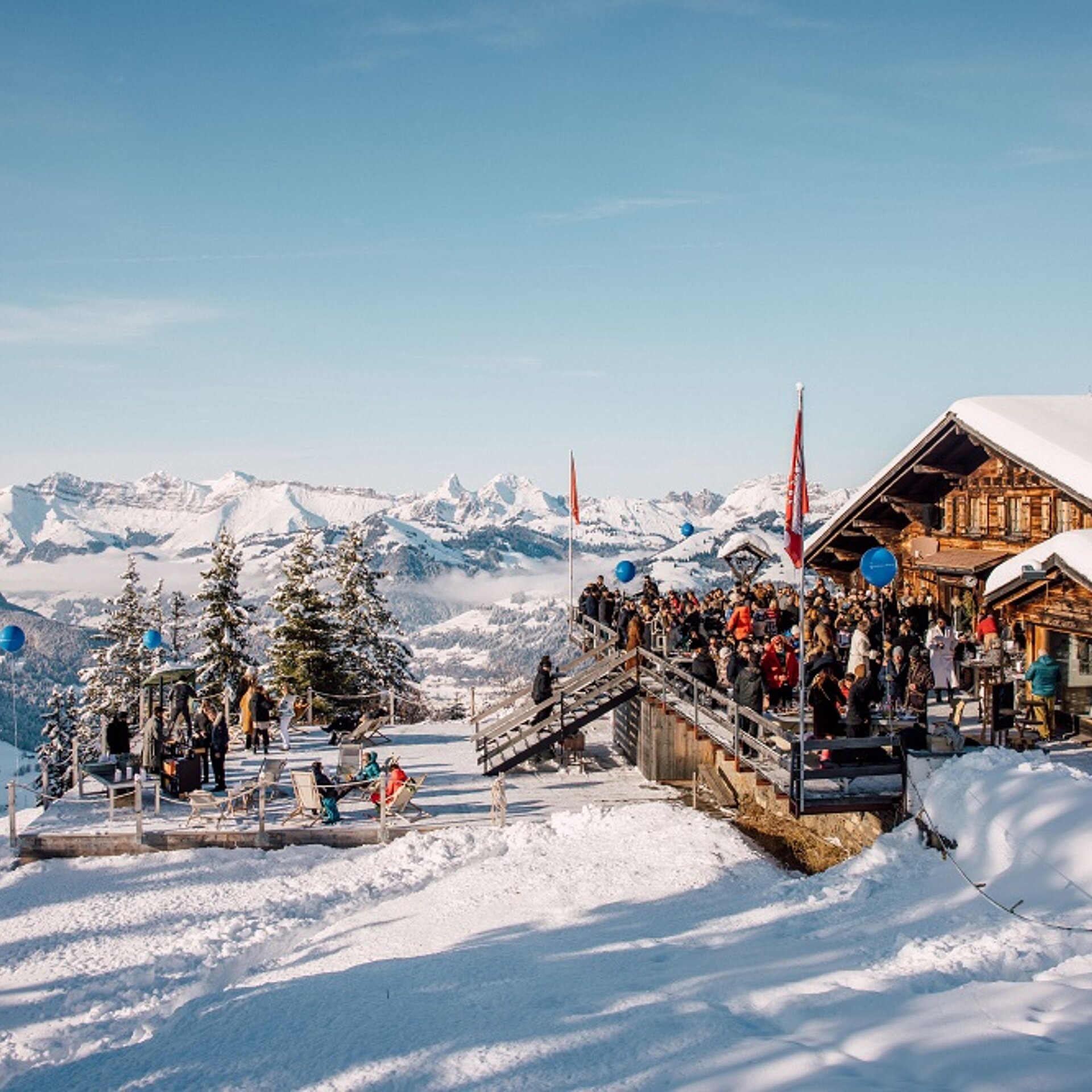Eine Gruppe von Menschen auf einer Terrasse im Schnee neben einem Bergrestaurant.