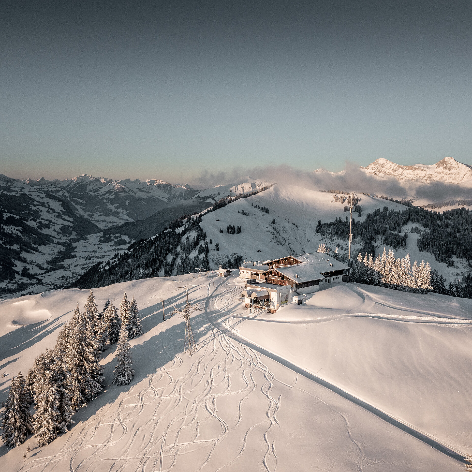 Luftaufnahme vom verschneiten Berghaus Rellerli inmitten einer verschneiten Berglandschaft.