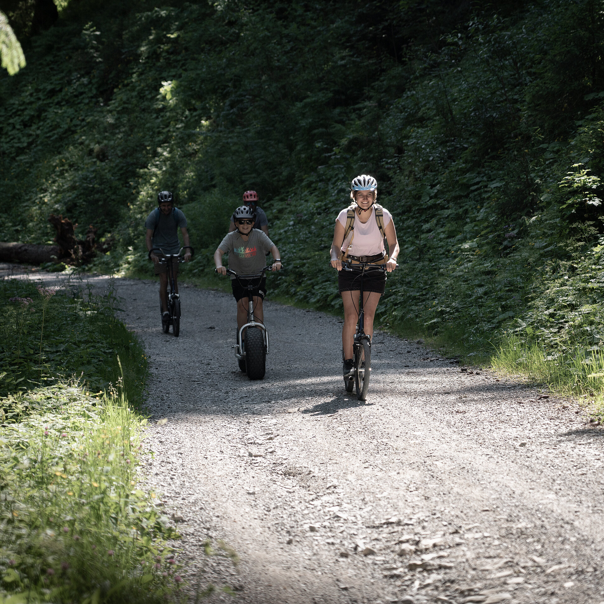 Personen fahren auf einem Trottinett den Berg runter bei sommerlicher Stimmung.