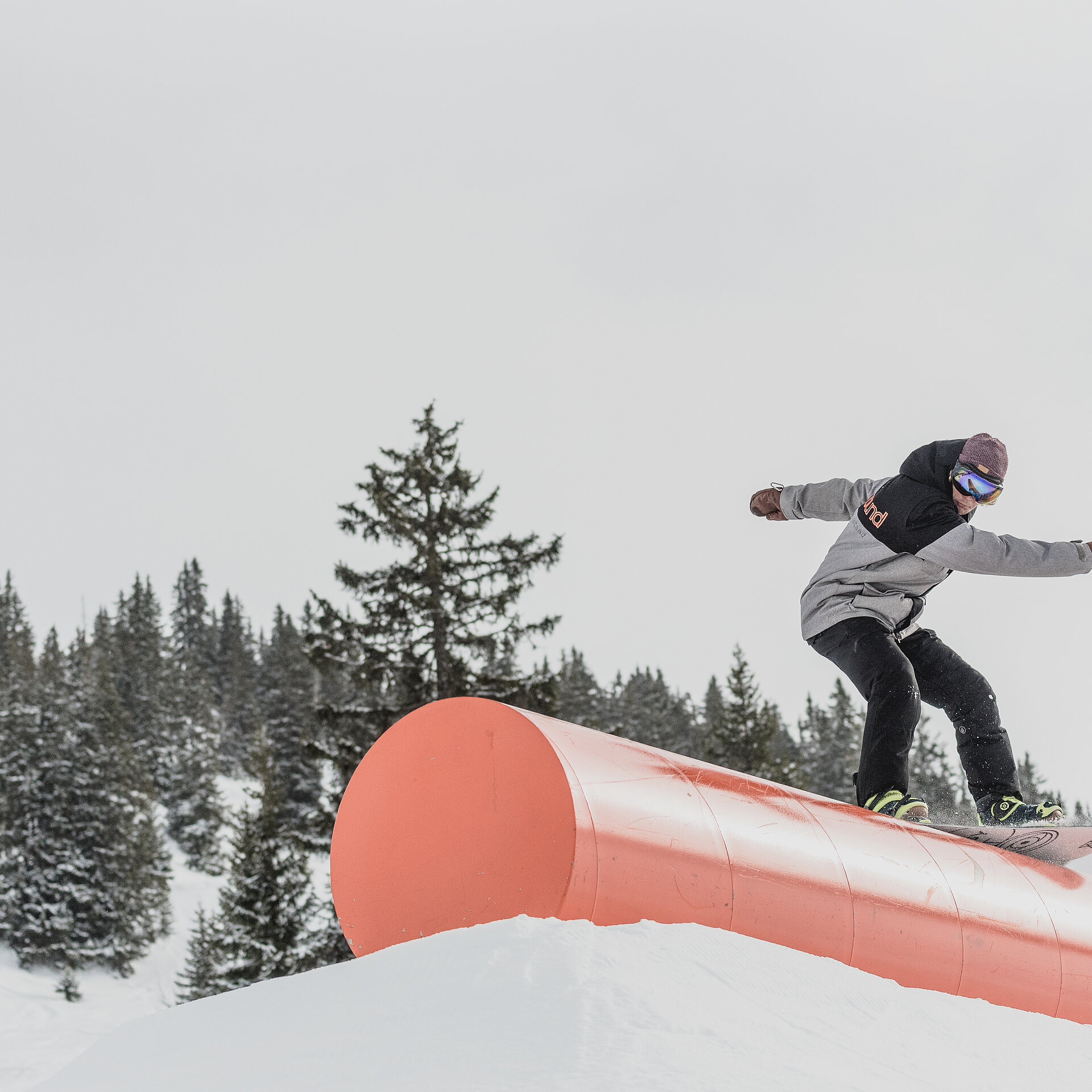 Ein dunkel gekleideter Snowboarder fährt über ein orangenes Rail im Snowpark.