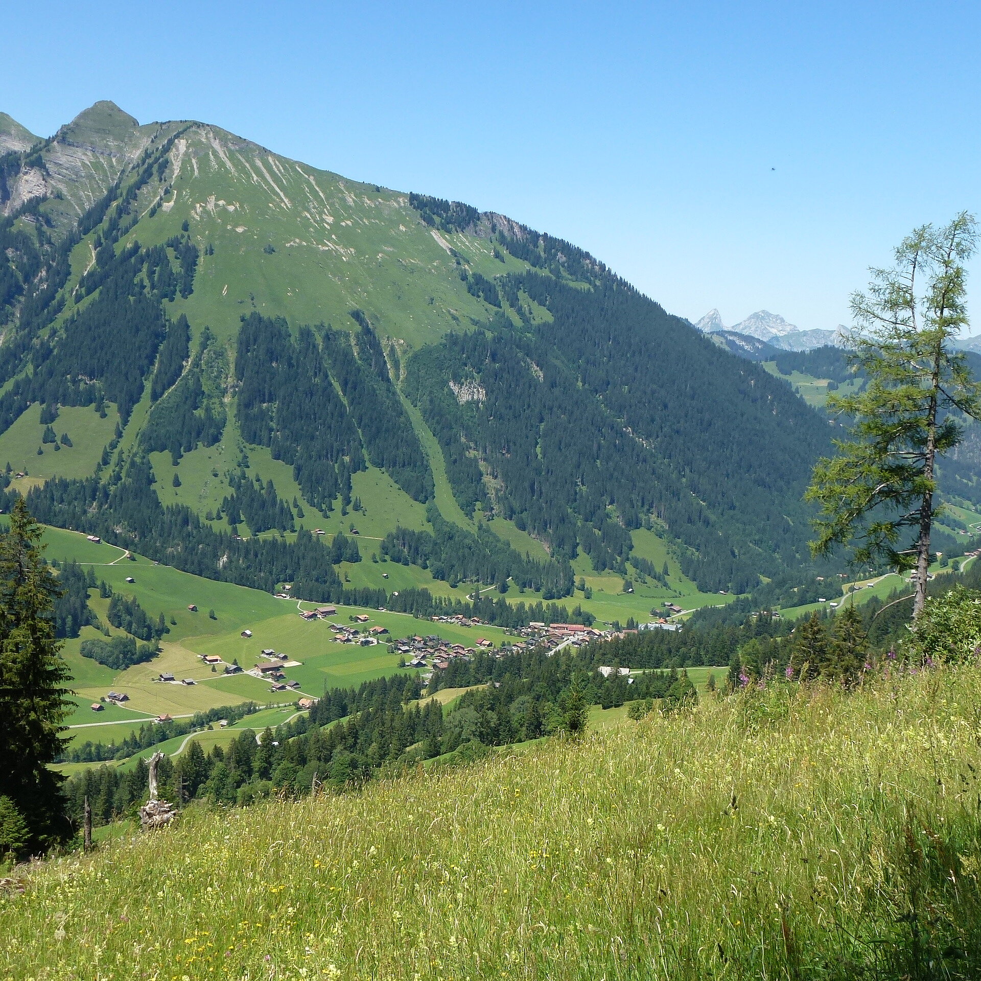 Blick auf ein grünes Tal mit einem kleine Dorf und vielen Bergen.