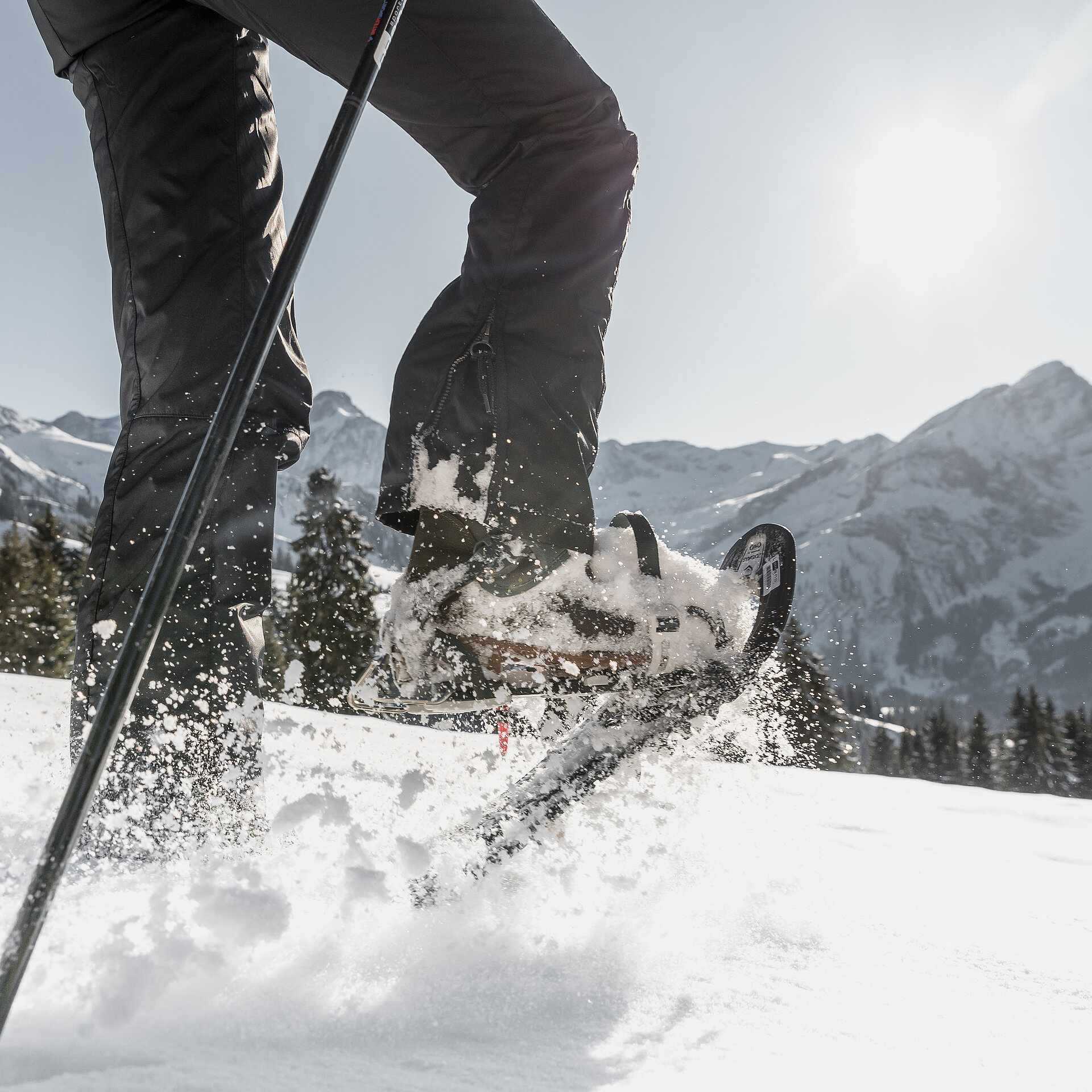 Männliche Beine welche mit Schneeschuhschuhen durch den Schnee stampfen vor herrlicher Bergkulisse.