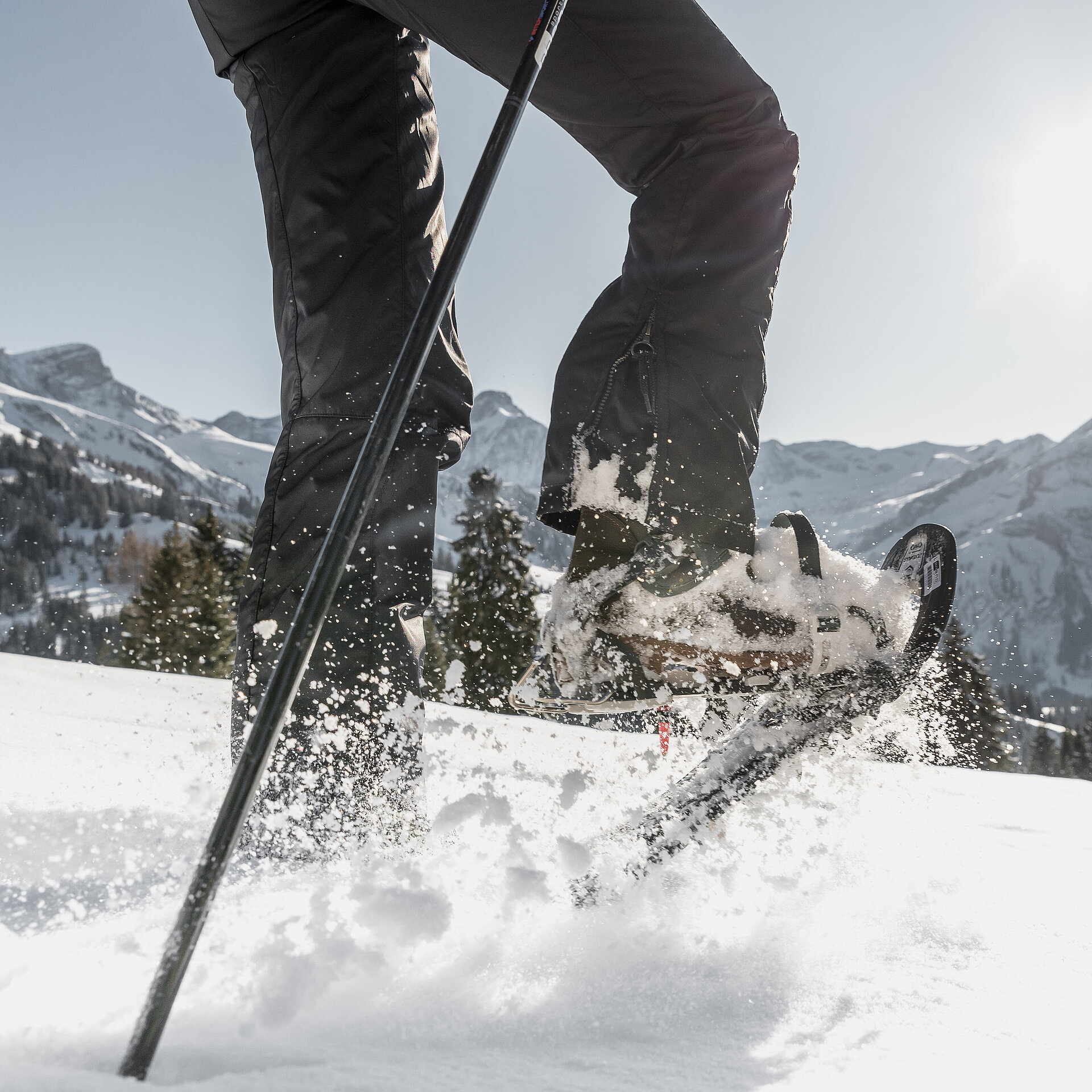 Männliche Beine welche mit Schneeschuhschuhen durch den Schnee stampfen vor herrlicher Bergkulisse.