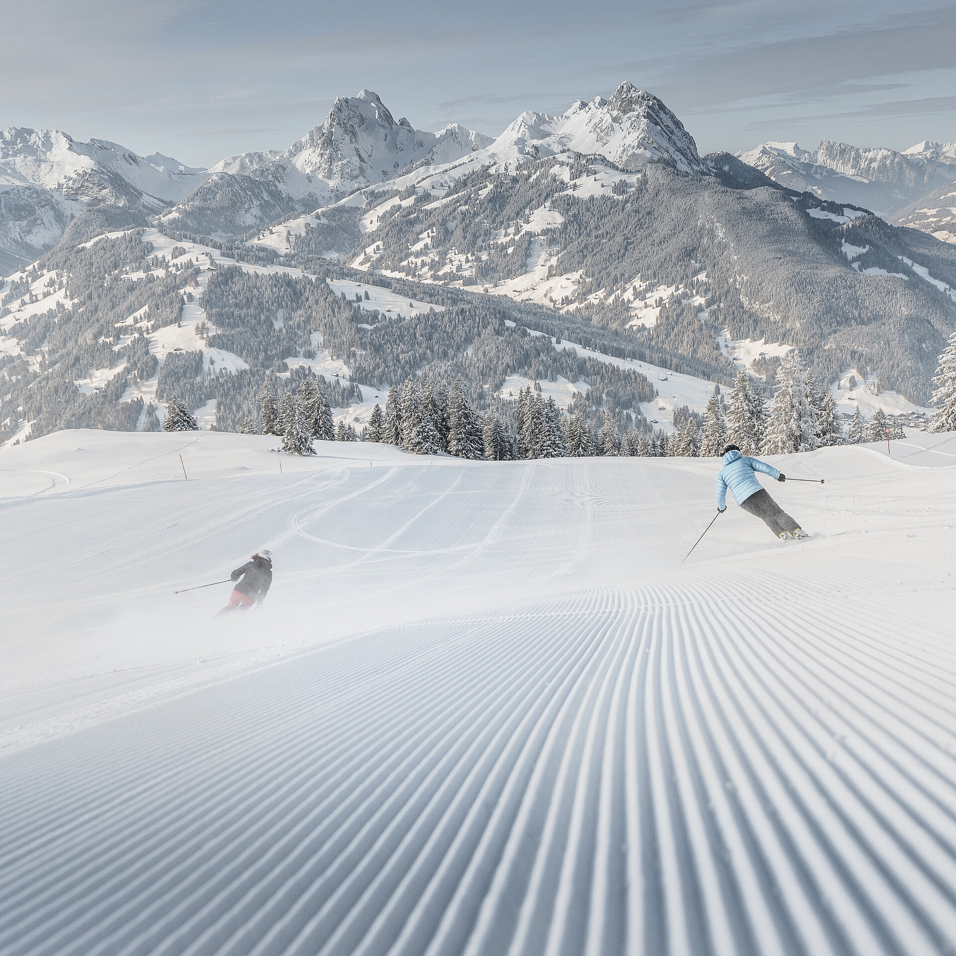 Weitsicht über die Skipiste mit 2 Skifahrern und verschneitem Bergpanorama.