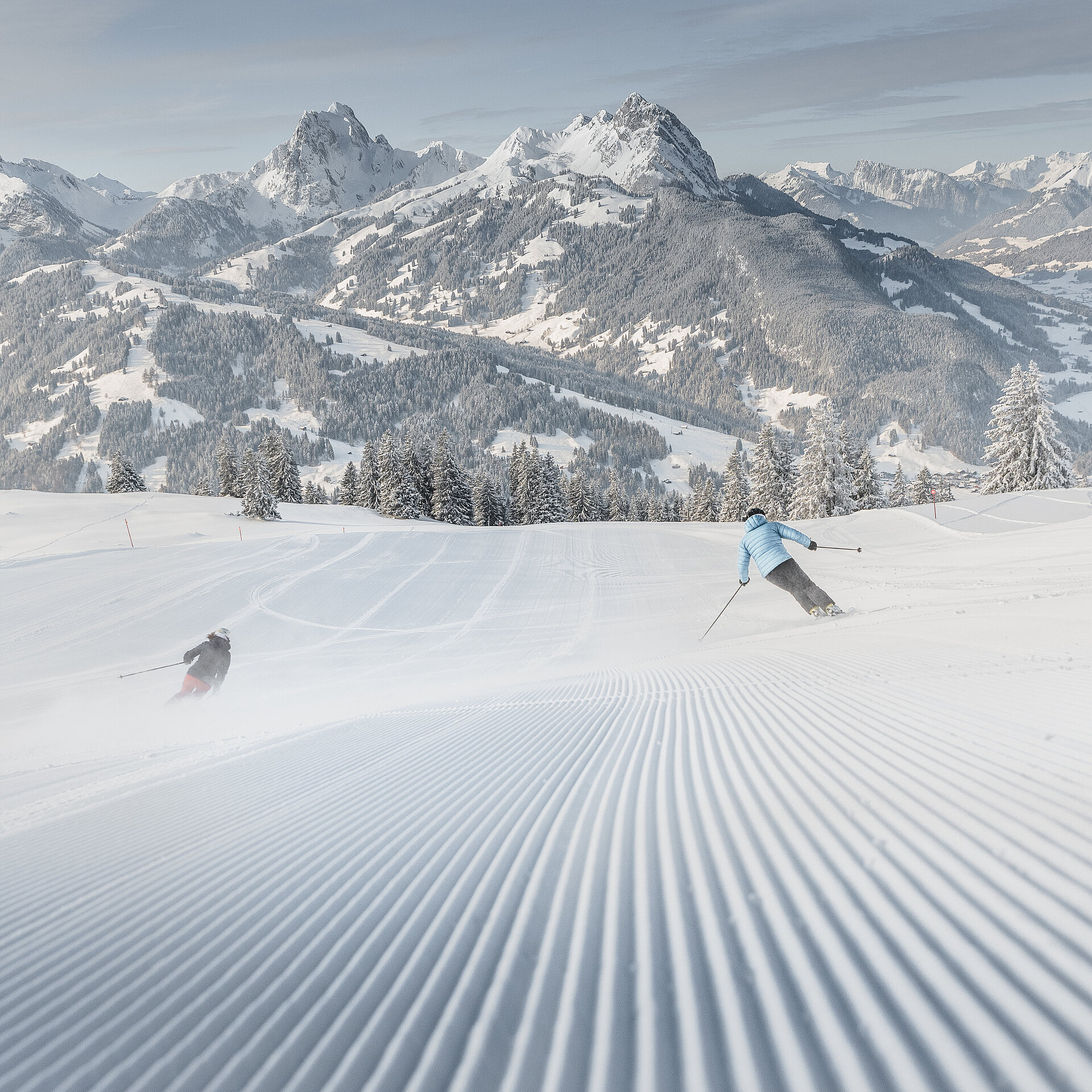 Weitsicht über die Skipiste mit 2 Skifahrern und verschneitem Bergpanorama.