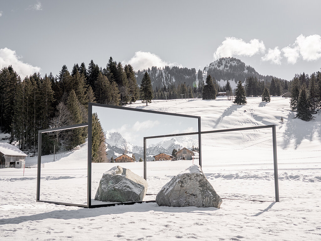 Kunstausstellung auf einer verschneiten Wiese mit Spiegeln und Steinen