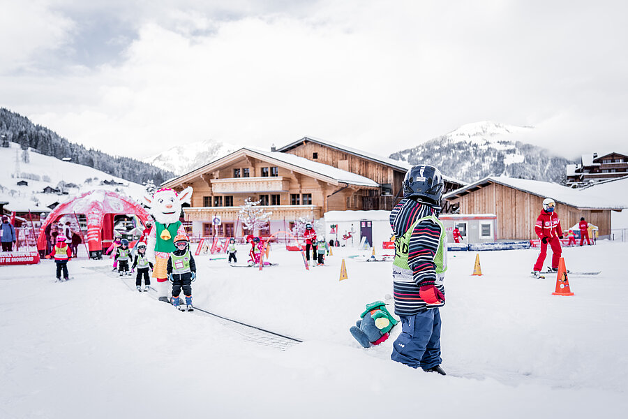 Reger Betrieb in Saanis Snowliand mit vielen Kindern auf Skis, Skilehrern und Saani auf der Skipiste im Tal.