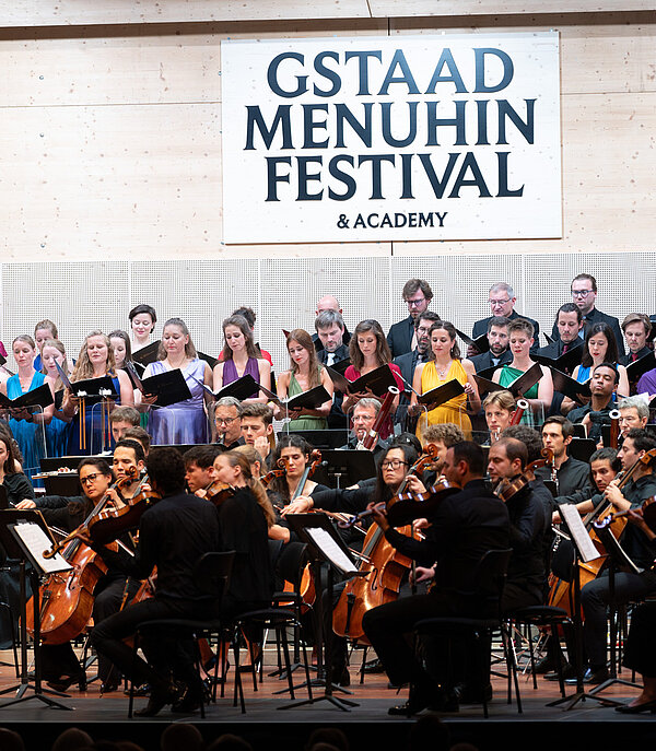 Orchester spielt auf einer Bühne. Im Hintergrund hängt ein Schild mit der Aufschrift Gstaad Menuhin Festival