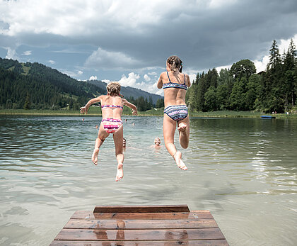 Zwei Kinder springen in den wunderschönen Bergsee Lauenensee.