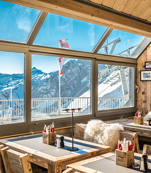 Tisch und Stühle im Bergrestaurant La Videmanette mit Blick auf eine verschneite Berglandschaft.