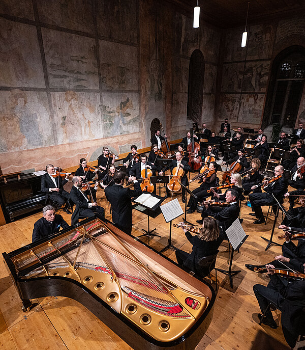 Ein Orchester spielt klassische Musik in einer Kirche mit christlichen Sujets an den Wänden.