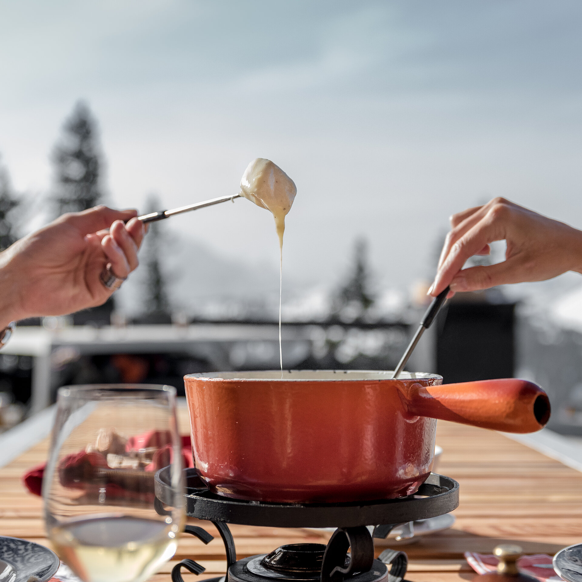 Roter Fondue Caquelon mit zwei Menschen-Hände beim Käsefondue essen.