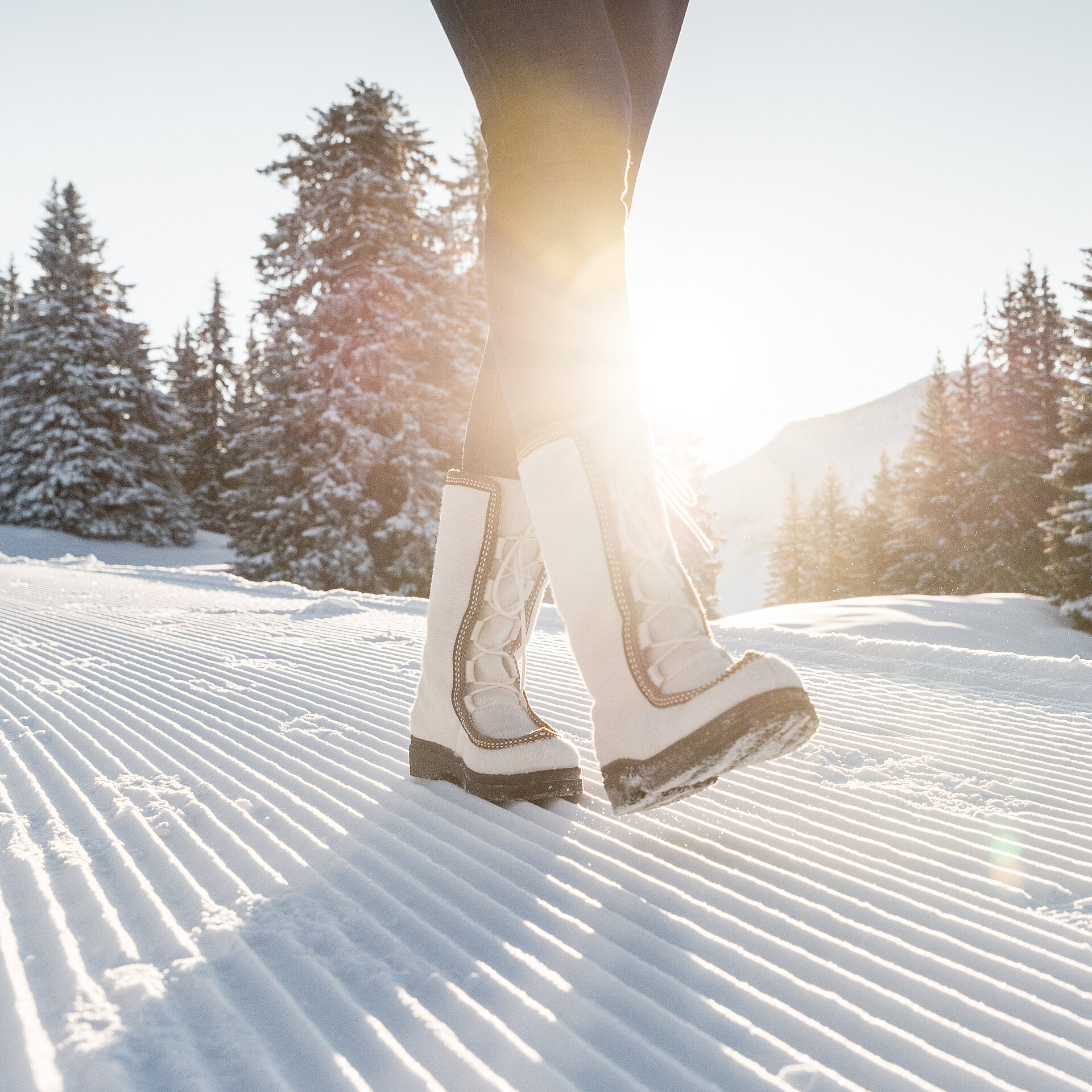 Weibliche Beine mit weissen Snowboots welche auf frisch präpariertem Winterwanderweg laufen.