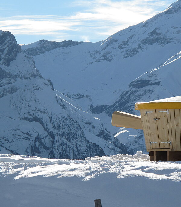 Hölzernes XXL Fondue Caquelon vor verschneitem Bergpanorama.