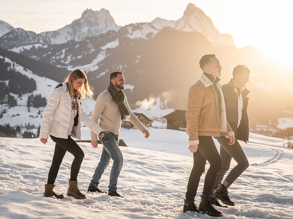 Personengruppe laufen auf einem Winterwanderweg mit verschneiter Bergkulisse.