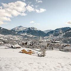 Blick auf das verschneite Dorf Saanen mit der Kirche und im Hintergrund Gstaad sowie Berge.