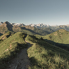 Ausblick auf die grüne und auf den Berggipfeln etwas verschneite Berglandschaft.