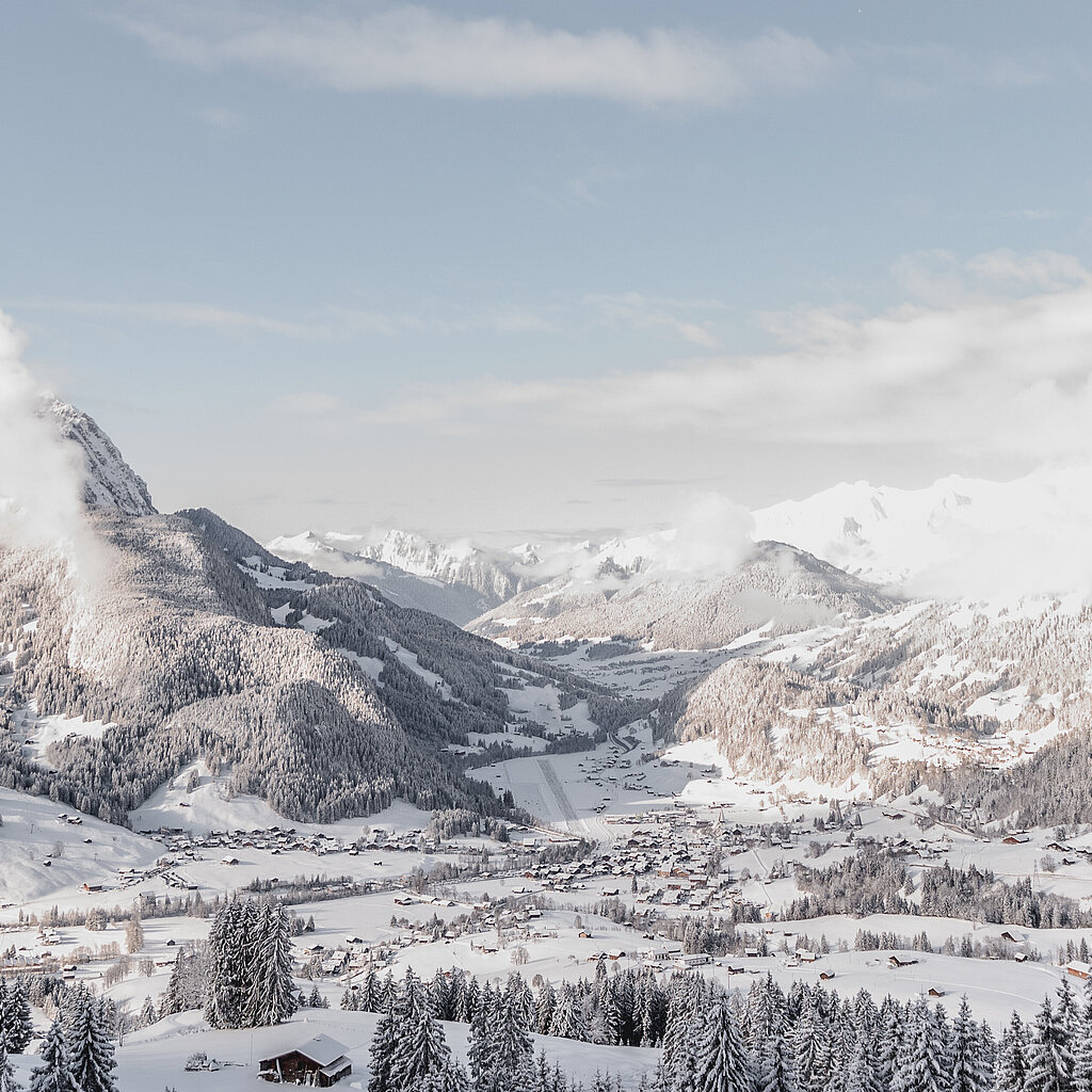 Panoramablick auf das winterliche Dorf Saanen mit dem Flugplatz und Bergen im Hintergrund.