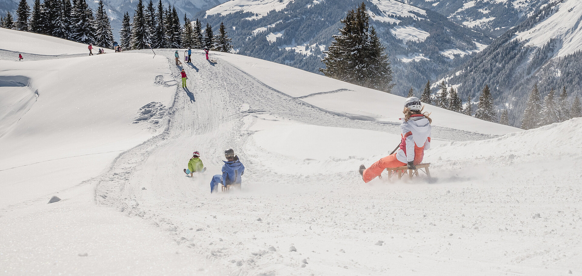 Schlittelnde Kinder inmitten verschneitem Bergpanorama.&nbsp;