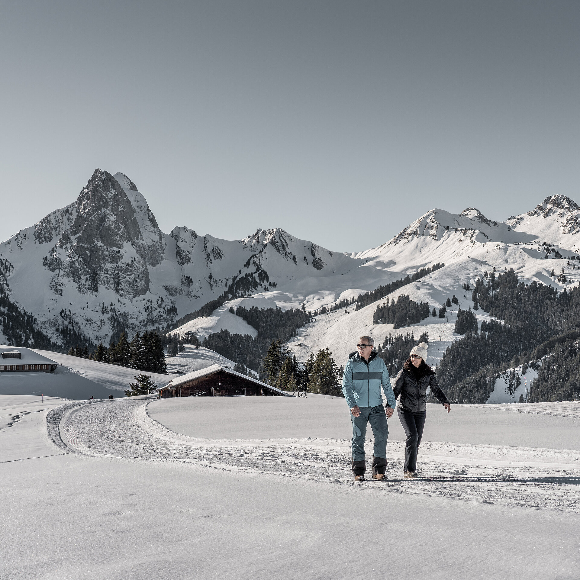 Pärchen wandert Hand in Hand auf einem Winterwanderweg mit verschneiter Bergkulisse