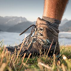 Nahaufnahme von Wanderschuhen welche im Gras stehen mit Bergen und Nebelmeer im Hintergrund.