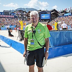 Turnierdirektor Ruedi Kunz vor dem Beachvolleyballfeld, im Hintergrund zahlreiche Zuschauer auf den Tribünen.