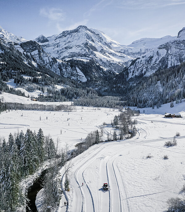 Drohnenaufnahme vom verschneiten Lauenen Tal im Winter. Im Hintergrund die verschneiten Berge.
